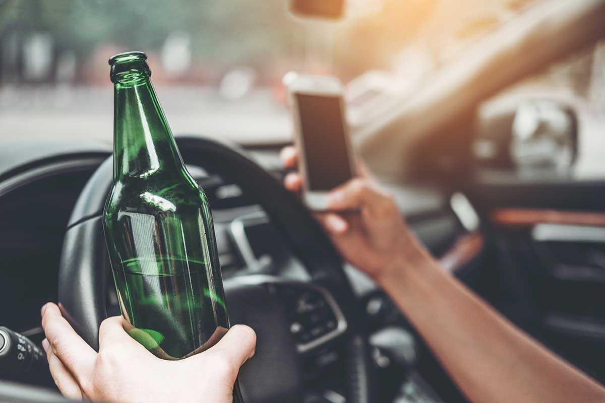 Bild von Fachgebietsseite Verkehrsrecht. Mann sitzt im Auto mit Smartphone und Bierflasche